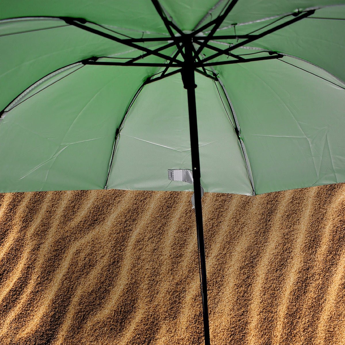 The underside of an open green umbrella reveals its black frame and silver lining, above a textured brown surface.